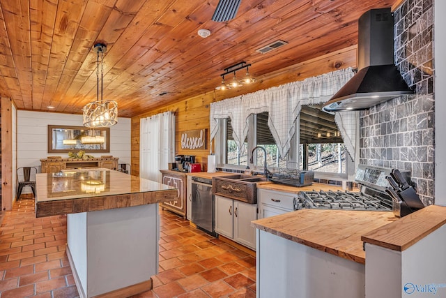 kitchen featuring appliances with stainless steel finishes, wooden walls, butcher block countertops, and wall chimney exhaust hood