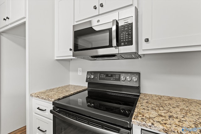 kitchen with light stone countertops, white cabinetry, and black electric range oven