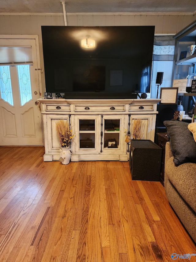 unfurnished living room with light wood finished floors, wooden walls, and ornamental molding