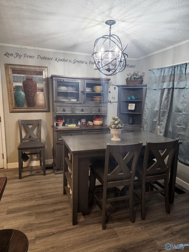 dining area with dark wood-style floors, a textured ceiling, an inviting chandelier, and ornamental molding