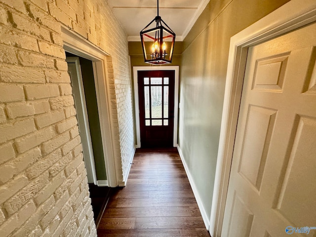 entryway featuring an inviting chandelier, ornamental molding, dark hardwood / wood-style floors, and brick wall