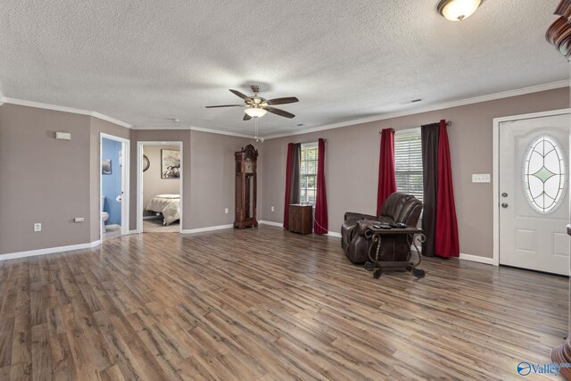 foyer entrance with ceiling fan, a textured ceiling, wood finished floors, baseboards, and ornamental molding