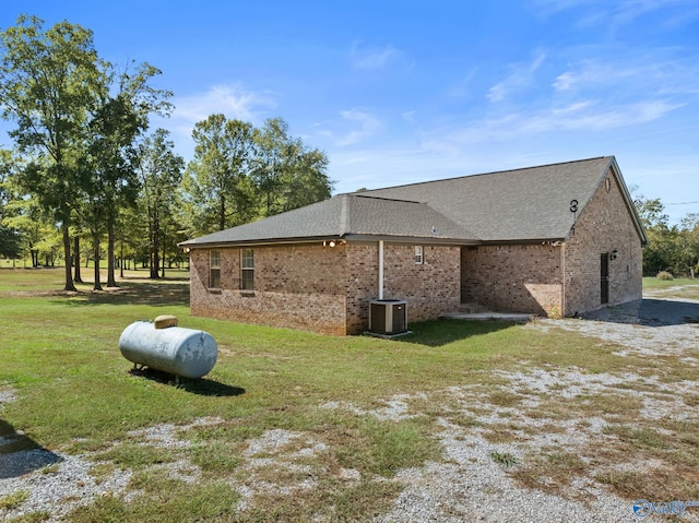 view of home's exterior featuring roof with shingles, brick siding, a lawn, and central air condition unit