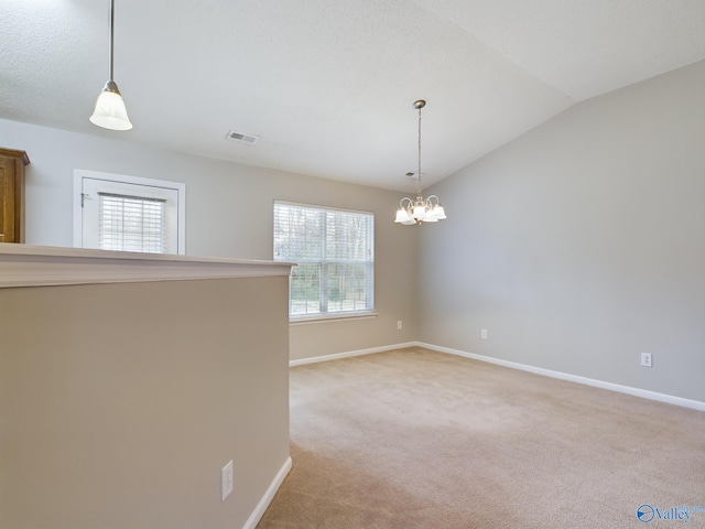 carpeted empty room with a wealth of natural light, vaulted ceiling, and an inviting chandelier