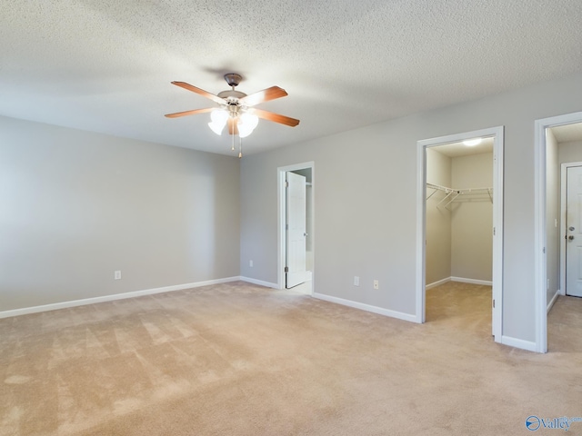 unfurnished bedroom with ceiling fan, a spacious closet, a textured ceiling, light colored carpet, and a closet