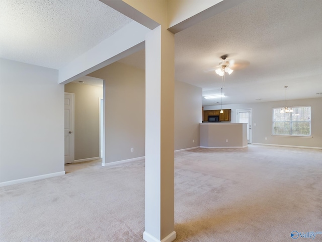 unfurnished living room featuring light carpet, ceiling fan with notable chandelier, and a textured ceiling