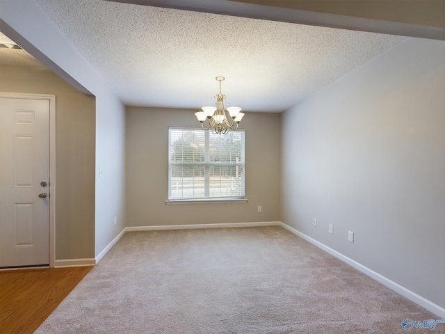 unfurnished room with a textured ceiling, carpet floors, and an inviting chandelier