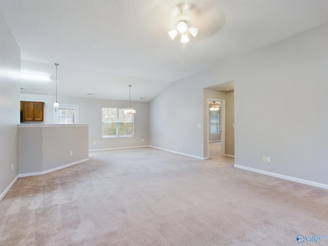 spare room with ceiling fan with notable chandelier, light colored carpet, and lofted ceiling