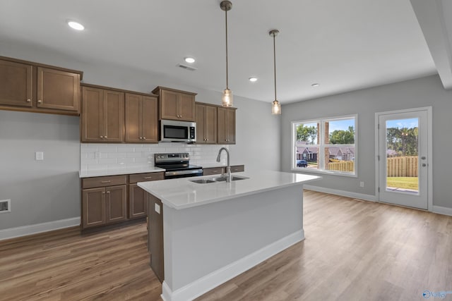 kitchen featuring pendant lighting, sink, backsplash, a kitchen island with sink, and stainless steel appliances