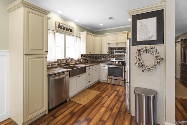 kitchen featuring dark wood-type flooring, sink, appliances with stainless steel finishes, cream cabinetry, and backsplash