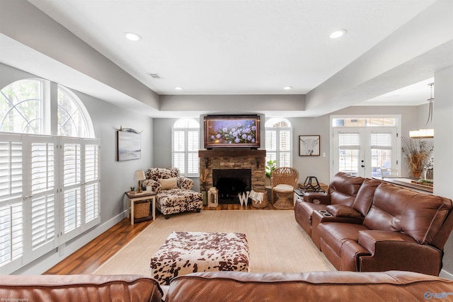 living room with a stone fireplace, french doors, and light wood-type flooring