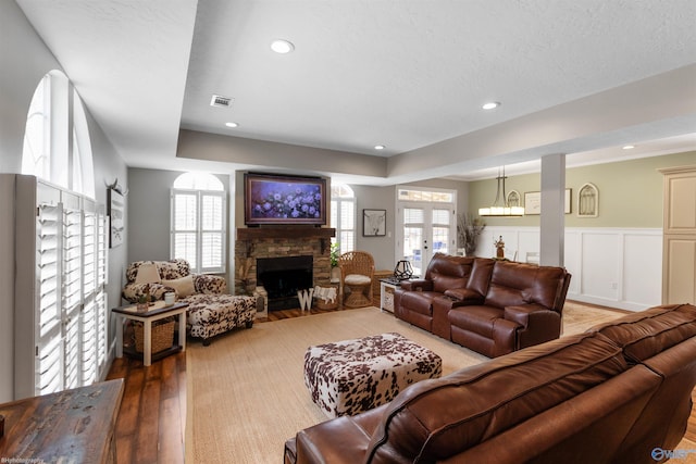 living room featuring french doors, a stone fireplace, a raised ceiling, and hardwood / wood-style floors