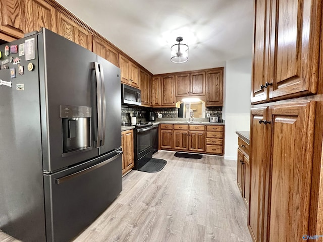 kitchen with brown cabinets, a sink, stainless steel appliances, light wood-type flooring, and backsplash