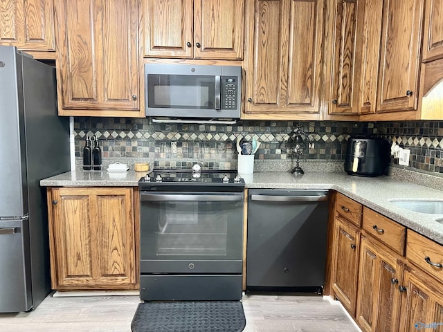 kitchen featuring light wood finished floors, decorative backsplash, appliances with stainless steel finishes, brown cabinets, and light countertops