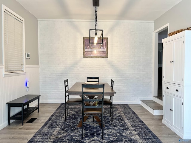 dining room featuring wainscoting, visible vents, brick wall, and wood finished floors