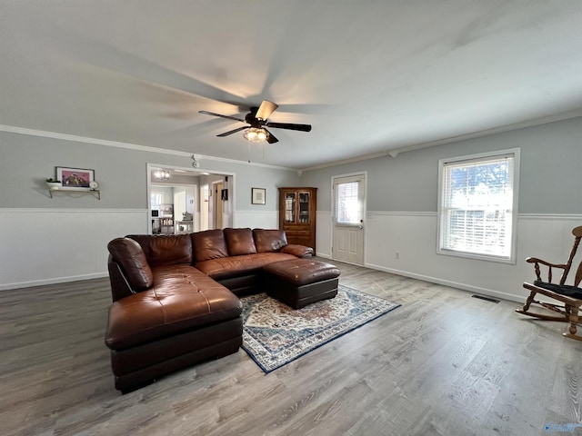 living area with visible vents, a ceiling fan, wainscoting, ornamental molding, and wood finished floors