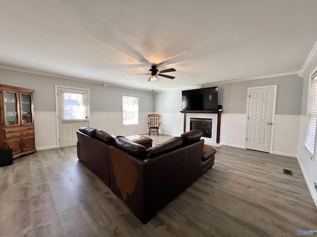 living room with visible vents, ornamental molding, a glass covered fireplace, wainscoting, and wood finished floors