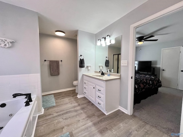 ensuite bathroom featuring ensuite bathroom, toilet, wood finished floors, vanity, and a tub with jets