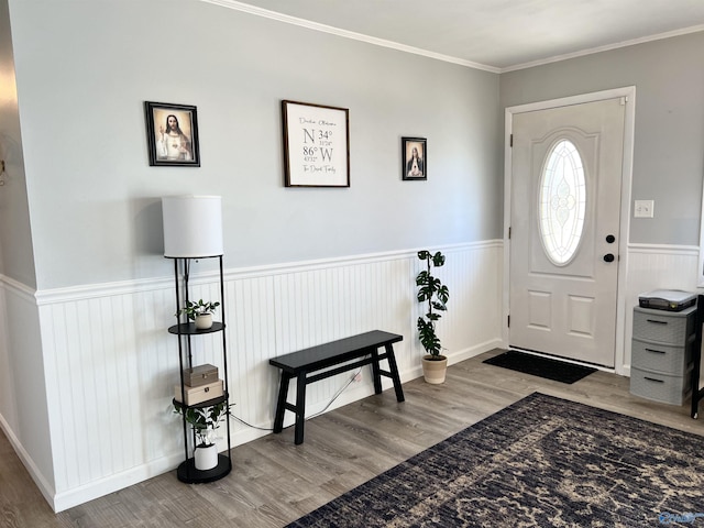 foyer entrance with a wainscoted wall, ornamental molding, and wood finished floors