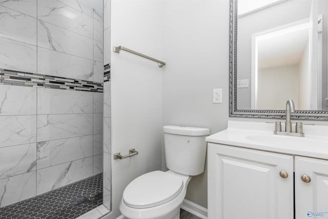 bathroom with toilet, baseboards, a tile shower, and vanity