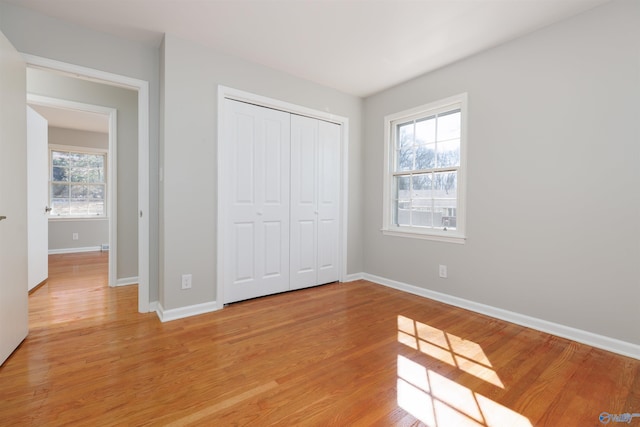 unfurnished bedroom featuring light wood-style flooring, baseboards, and a closet