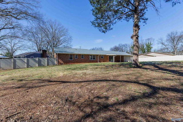 rear view of house with brick siding, a lawn, and fence