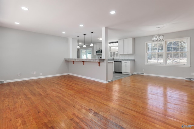 kitchen featuring a kitchen breakfast bar, open floor plan, a peninsula, stainless steel appliances, and white cabinetry