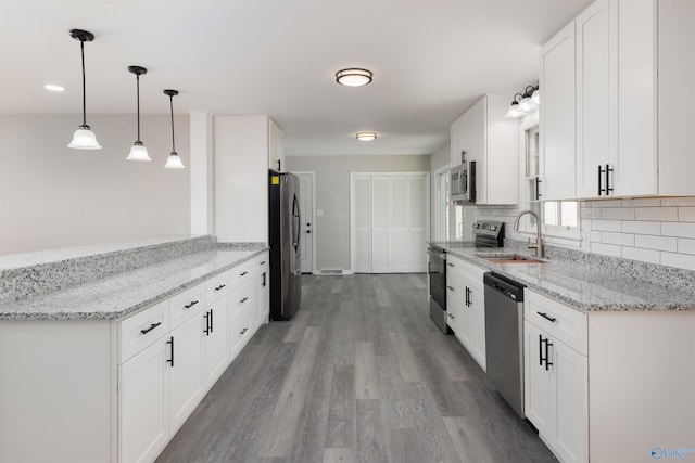 kitchen with light stone counters, decorative light fixtures, appliances with stainless steel finishes, white cabinetry, and a sink