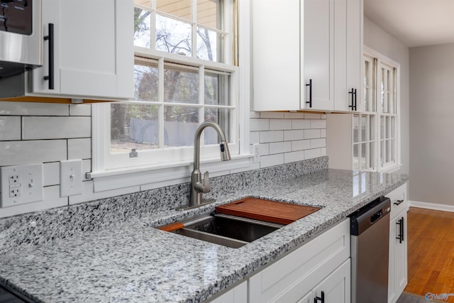 kitchen featuring stainless steel dishwasher, a sink, light stone countertops, and white cabinets