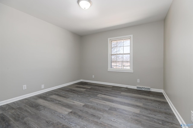 unfurnished room featuring baseboards, visible vents, and dark wood finished floors