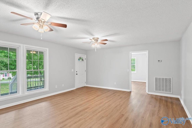 empty room featuring wood finished floors, a ceiling fan, a textured ceiling, visible vents, and baseboards