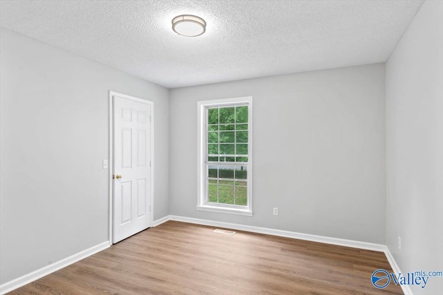 spare room featuring a textured ceiling, baseboards, visible vents, and wood finished floors