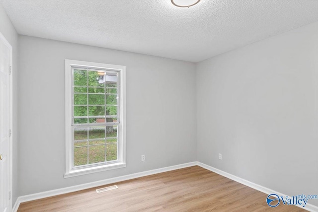 empty room with light wood-style flooring, a textured ceiling, baseboards, and visible vents