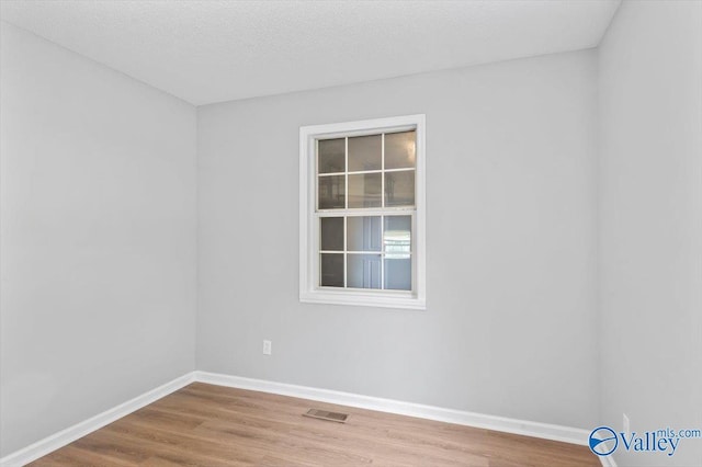 empty room with a textured ceiling, visible vents, wood finished floors, and baseboards