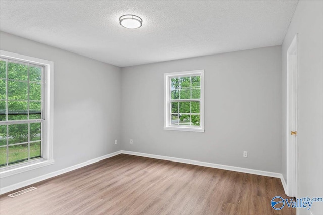 unfurnished room with baseboards, visible vents, a textured ceiling, and wood finished floors