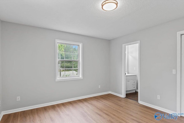unfurnished bedroom with baseboards, connected bathroom, a textured ceiling, and wood finished floors