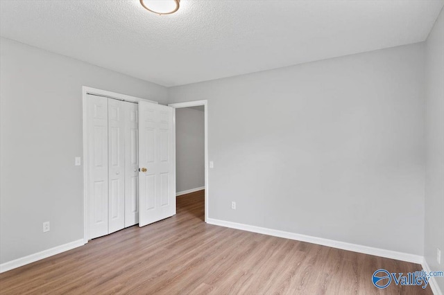 unfurnished bedroom featuring a textured ceiling, baseboards, a closet, and wood finished floors