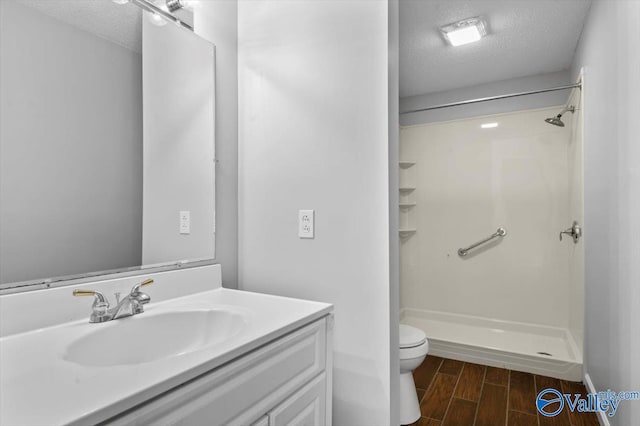 bathroom with toilet, a textured ceiling, wood finish floors, walk in shower, and vanity