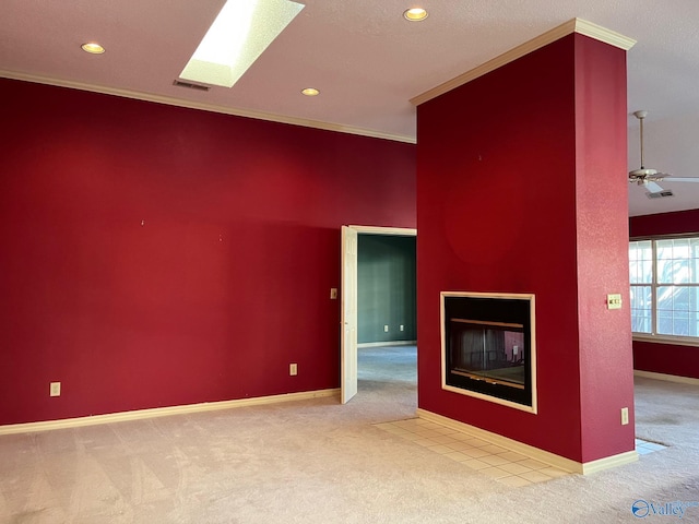 unfurnished living room featuring a skylight, ceiling fan, light colored carpet, and ornamental molding