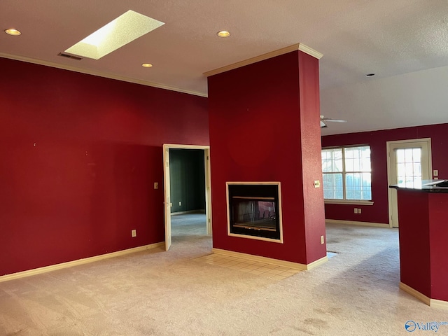 empty room with a multi sided fireplace, a skylight, crown molding, and light colored carpet