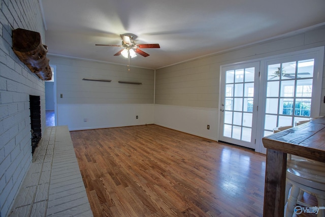 unfurnished living room featuring a ceiling fan, a brick fireplace, and wood finished floors