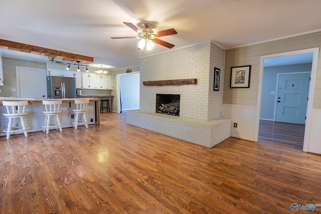 unfurnished living room with ornamental molding, ceiling fan with notable chandelier, a fireplace, and wood finished floors