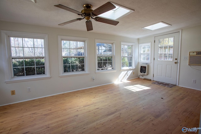 unfurnished sunroom with a skylight, a wall unit AC, ceiling fan, and heating unit