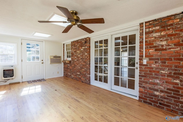 interior space with heating unit, light wood-style flooring, a wall mounted AC, ceiling fan, and brick wall