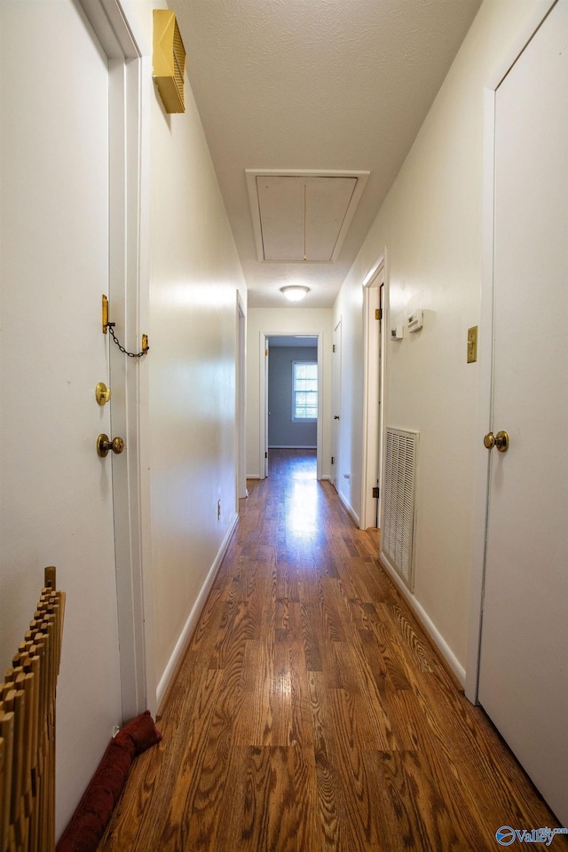 hall featuring dark wood-style flooring, visible vents, baseboards, radiator heating unit, and attic access