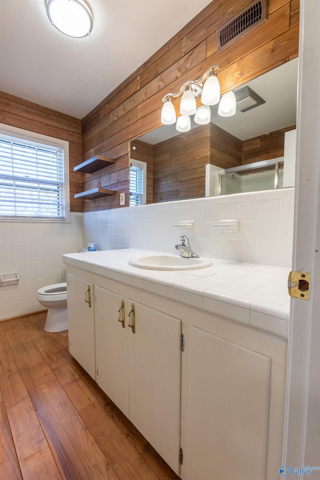 full bathroom featuring visible vents, decorative backsplash, an enclosed shower, vanity, and wood finished floors