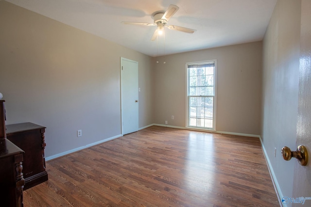 unfurnished room with a ceiling fan, baseboards, and dark wood-type flooring