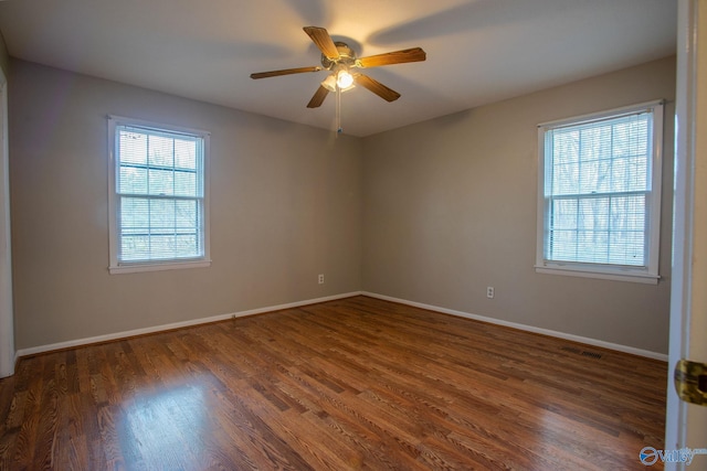 empty room featuring baseboards, dark wood-style flooring, visible vents, and a healthy amount of sunlight