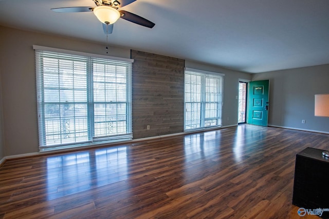 unfurnished living room with ceiling fan, baseboards, and dark wood-style flooring