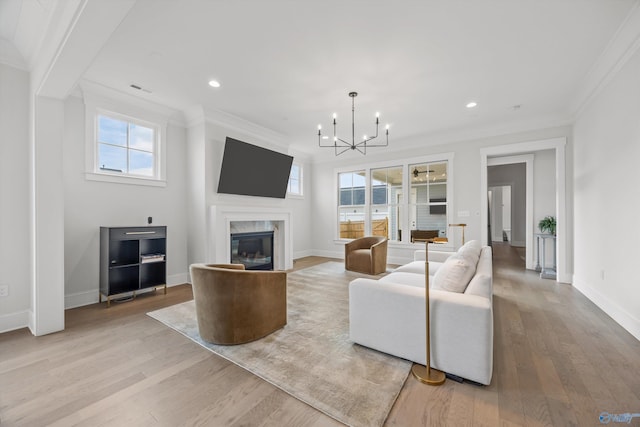 living room featuring light hardwood / wood-style flooring, a high end fireplace, ornamental molding, and an inviting chandelier